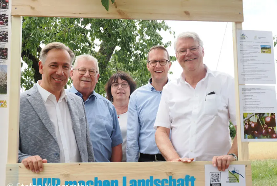 Menschengruppe in Holzrahmen vor Kirschwiese