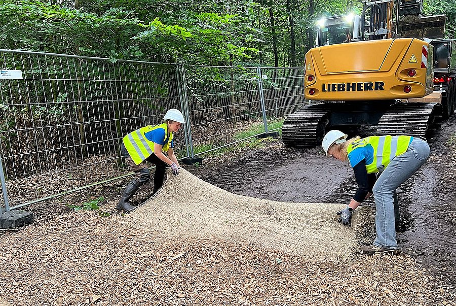 Zwei Frauen verlegen Matten mit Hackschnitzel bedeckt.