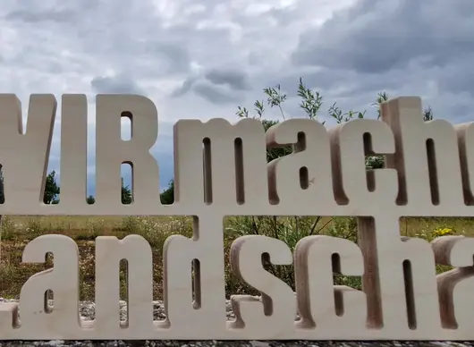 WIR machen Landschaft Schriftzug vor bewölktem Himmel