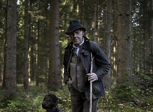 Josef Göppel steht im Wald, nehmen ihm sitzt sein Jagdhund Akso.