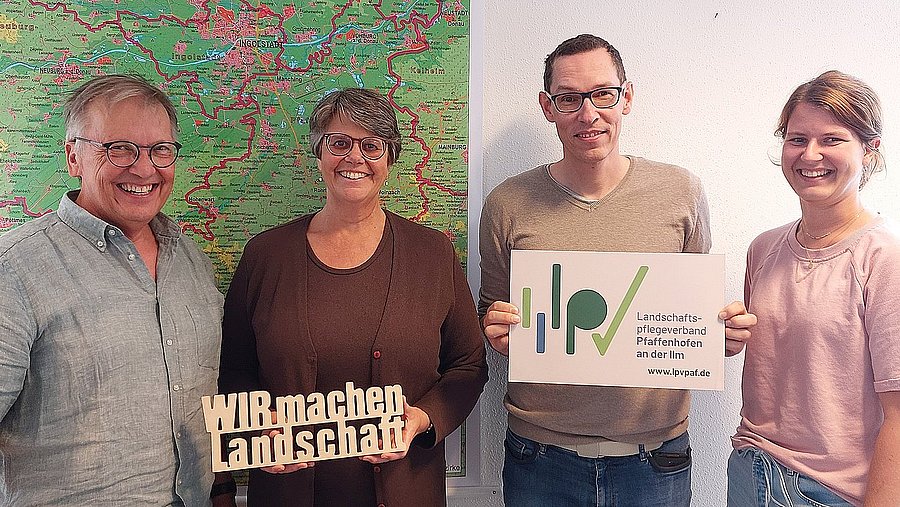 Vier Personen vor einer Landkarte mit Holzschild „WIR machen Landschaft“ und LPV-Logo