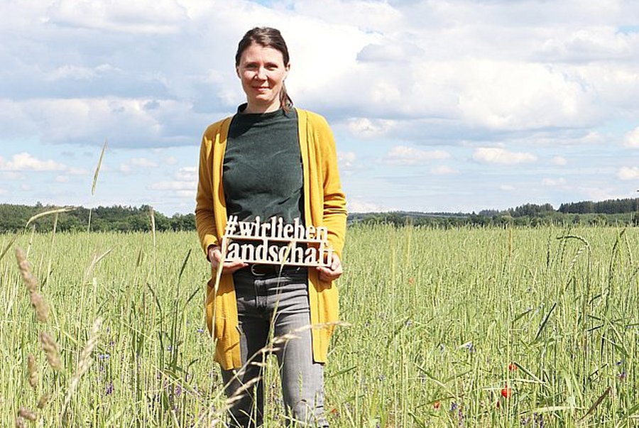 Maike Fischer vom DVL steht in einem Acker mit blühenden Ackerwildkräutern.