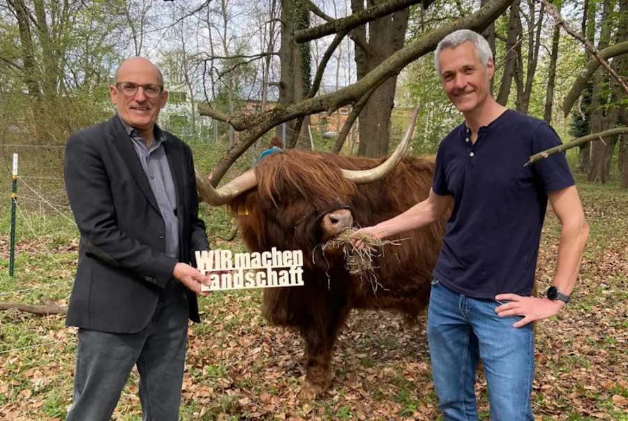 2 Männer halten einen Schriftzug vor einem Hochlandrind