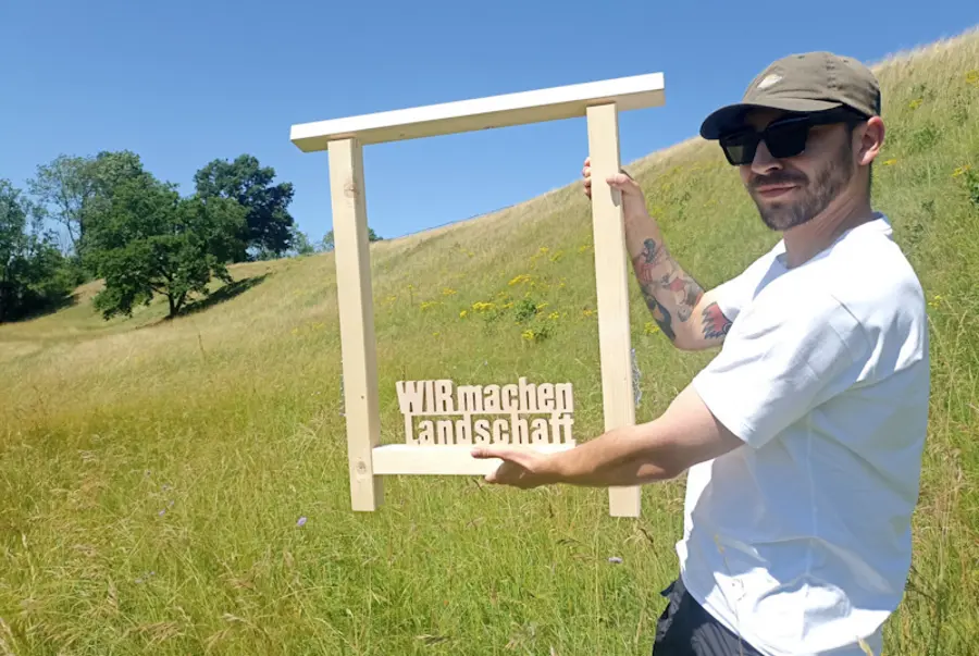 Person mit Holzrahmen vor blühender Wiese
