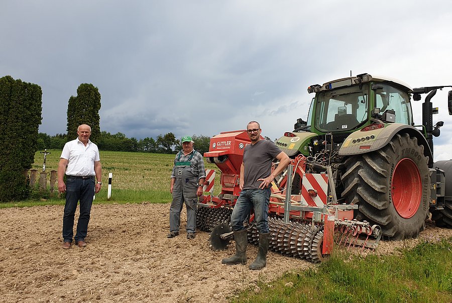 Drei Männer stehen auf einer Wiese vor einer landwirtschaftlichen Maschine