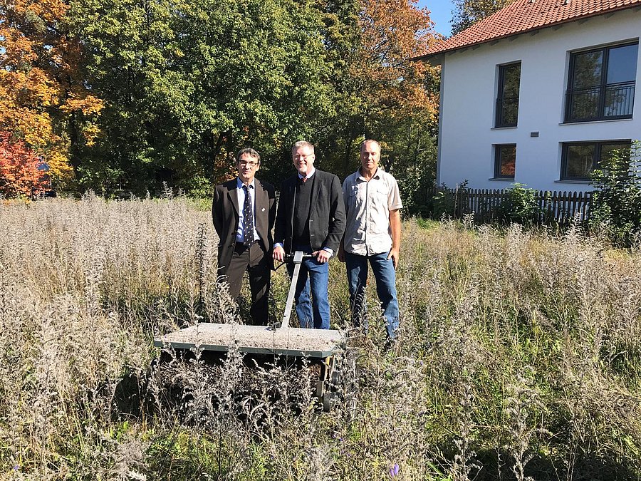 Drei Personen stehen auf einer Wiese und ernten mit einer Maschine Saatgut.