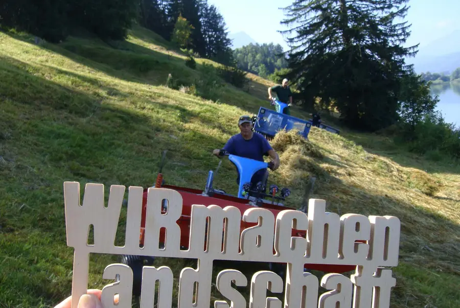 Schriftzug vor 2 Mäher am Hang